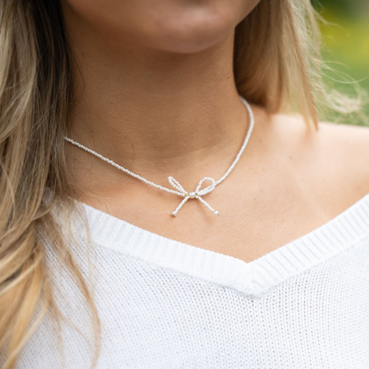 Person wearing a white choker necklace with a bow pendant against a blurred green background