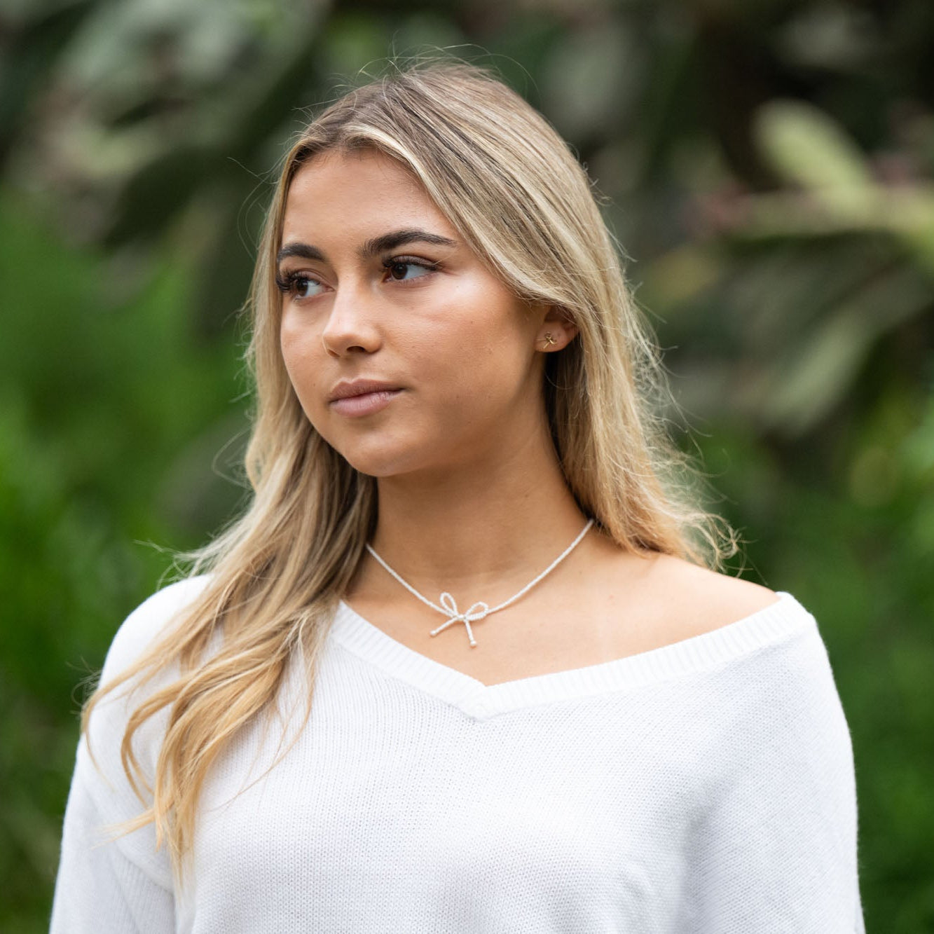 Person wearing a white choker necklace with a bow pendant against a blurred green background