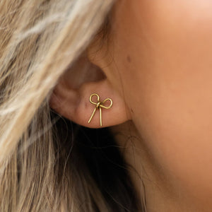handmade bow studs brass gold Simple yet meaningful, these dainty hand-forged bows are perfect for everyday wear. Symbolizing resilience and strength, the bow serves as a reminder of lives beautifully tied together through hope and freedom. Each stud is carefully shaped by hand and finished with sterling silver posts for comfort and durability.

Hand-cut, hammered, and assembled by a young woman in India rebuilding her life after human trafficking, every pair carries her story of courage and dignity. Your p