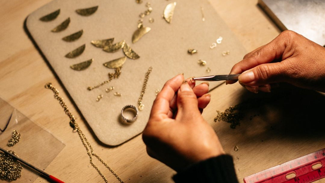 Person working on jewelry with tools and materials on a wooden surface