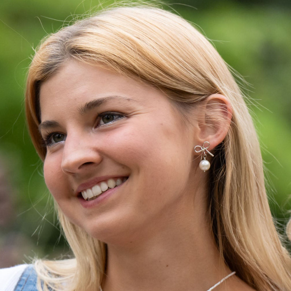 Delicate and timeless, our hand-forged Pearl Bow Studs are perfect for everyday wear. Each stud features a handcrafted brass bow paired with a luminous pearl, securely finished with sterling silver posts.

Every detail—from cutting and hammering to final assembly—is carefully done by a young woman in India rebuilding her life after human trafficking. With each purchase, you support her journey toward hope, dignity, and a brighter future through our non-profit, International Sanctuary.